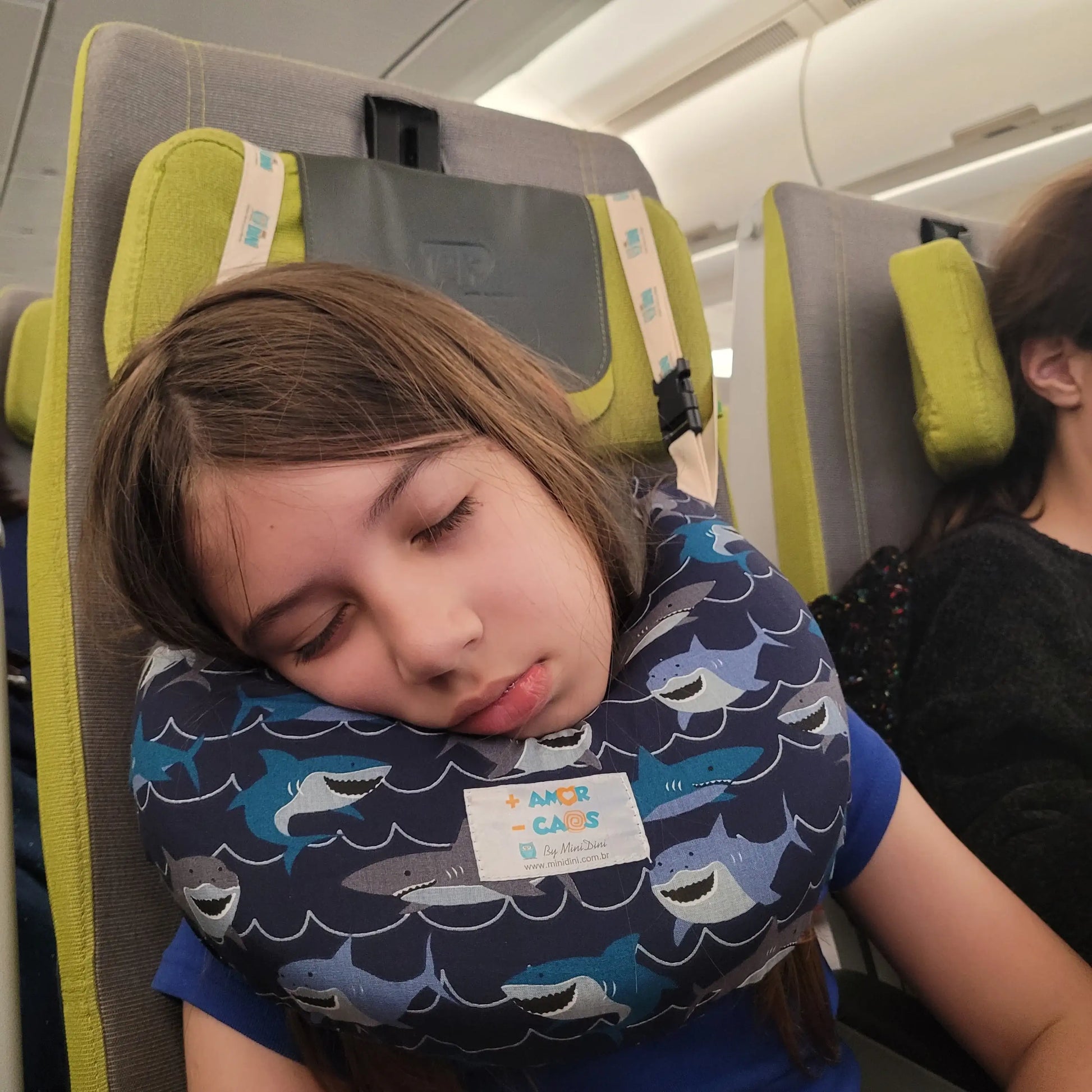 Foto 2: Criança dormindo com travesseiro de viagem Nanadini no avião.Almofada de viagem infantil Nanadini sendo usada por uma criança dormindo no assento de avião, garantindo suporte cervical e conforto no voo.